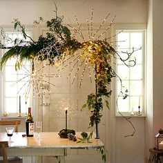 a dining room table with candles and plants on it, next to a wine bottle