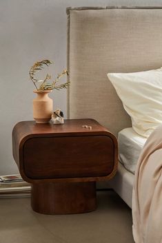 a bed with a wooden night stand next to it and a plant on the nightstand