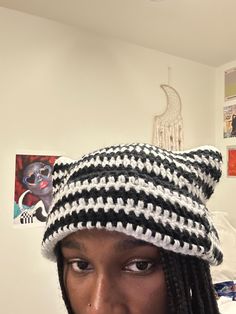 a young man wearing a crocheted hat in his bedroom with pictures on the wall behind him