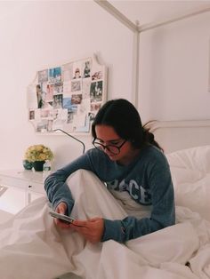 a woman sitting on top of a bed looking at her cell phone while wearing glasses