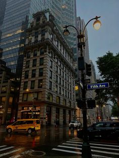 an intersection in the city at dusk with cars driving by and tall buildings on either side