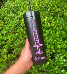 a hand holding a black tumbler cup with a pink syringe on it