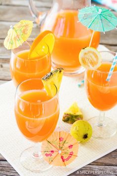 three glasses filled with orange juice on top of a white place mat next to an umbrella