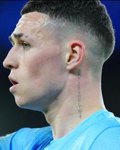 a close up of a person with a shaved head and tattoos on his neck, wearing a blue shirt