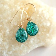 two green earrings sitting on top of a piece of white rock next to a pair of gold filled ear wires