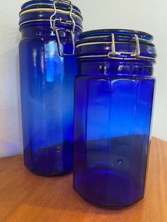 two blue glass jars sitting on top of a wooden table next to eachother