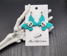 pair of skull and crossbones earrings with turquoise colored material on wooden table next to skeleton's leg