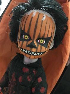 a creepy doll with black hair and orange eyes sitting in front of an orange bag