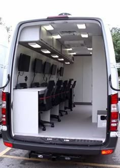 the back end of a white van filled with black chairs and desks in an empty parking lot