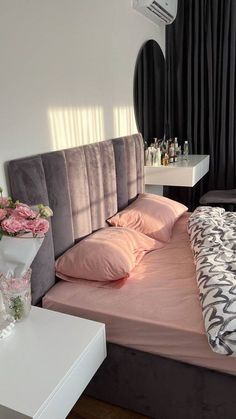 a bed with pink sheets and pillows next to a white table in front of a mirror