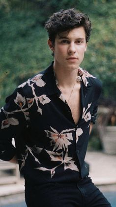 a young man wearing a black shirt with white flowers on it is posing for the camera