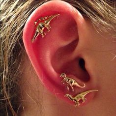 three small dinosaurs are attached to the side of a woman's ear with gold colored posts