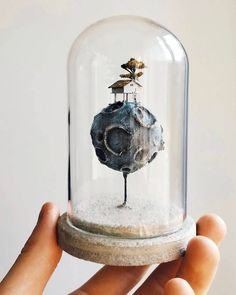 a hand holding up a glass dome with a small tree on top in the middle