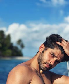 a shirtless man standing in front of the ocean with his hand on his head