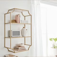 a shelf with books and other items on it in front of a white wall next to a window