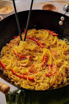 noodles being cooked in a wok with chopsticks on the side and seasoning