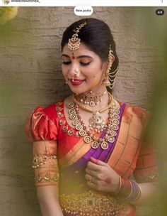 a woman in an orange and pink sari with gold jewelry on her neck, standing next to a brick wall