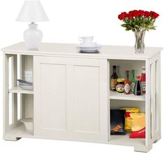 a white cabinet with flowers and plates on it's shelf next to a vase filled with red roses