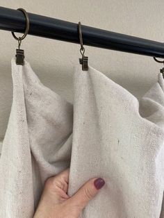 a person's hand is on the curtain rod in front of a white cloth