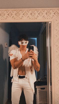 a man with white makeup and angel wings taking a selfie in front of a mirror