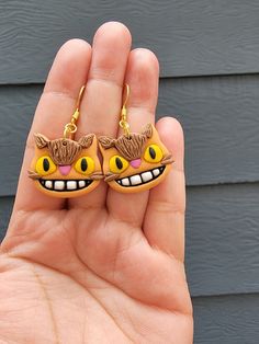 a hand holding two yellow earrings with cats on it's ears and eyes,