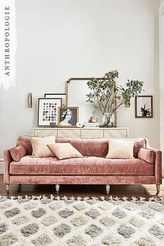 a living room with a pink velvet couch and some framed pictures on the wall above it