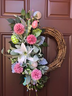 a wreath with pink flowers and green leaves is hanging on the front door's brown door