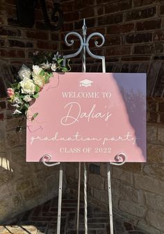 a welcome sign with flowers on it in front of a brick wall