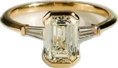 an emerald and diamond ring with three baguets on the side, set in yellow gold