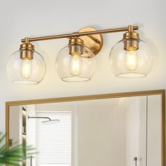 three light bathroom fixture with clear glass globes and gold trim on the vanity mirror