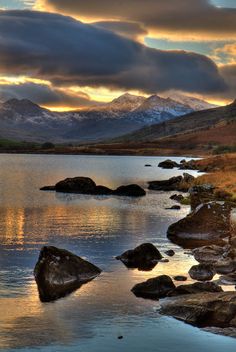 the mountains are reflected in the still water at sunset, as clouds loom over them