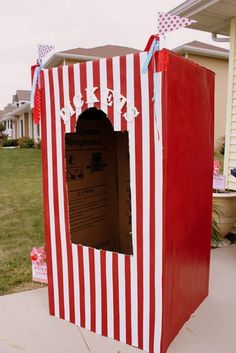 a red and white striped cardboard box with a door open in front of a house