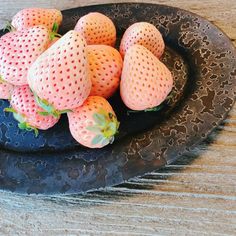 a black plate filled with strawberries on top of a wooden table