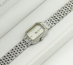 This silver-colored watch boasts a rectangular case surrounded by stones, adding a touch of elegance and sparkle. The grey metallic dial is also adorned with stones, enhancing its luxurious appeal. Paired with a classic metal bracelet, the watch strikes a balance between simplicity and brilliance. It's a sleek, bright, and elegant accessory that stands out for its understated glamour and sophistication. Dimensions: Bracelet Length: up to 16 cm (6.3 inches) - adjustable Case Width: 1.7 cm (0.4 inches) Case Height: 2.3 cm (0.9 inches) Bracelet Width: 1 cm (0.4 inches) Condition: The watch is in good condition, with minor wear on the bracelet and a tiny chip on the glass between the 3 and 4-hour marks, details in the photo. All presented watches are tested and in working condition, also equip Silver Rectangular Diamond Watch For Anniversary, Silver Diamond Watch With Diamond Accents As Gift, Timeless Silver Rectangular Diamond Watch, Elegant Stainless Steel Diamond Watch With Accents, Elegant Stainless Steel Diamond Watch With Diamond Accents, Elegant Diamond Watch With Rectangular Stainless Steel Dial, Silver Diamond Watch With Rectangular Dial For Evening, Rectangular Diamond Watch As A Gift, Rectangular Diamond Watch As Gift