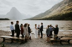 a group of people standing next to each other near a body of water with mountains in the background