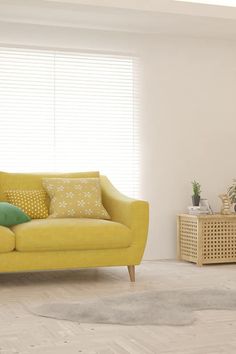 a living room with yellow couches and green pillows on the floor, in front of a window