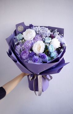 a bouquet of purple and white flowers is being held by someone's hand,