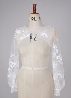 a mannequin is wearing a white dress with sheer sleeves and flowers on it