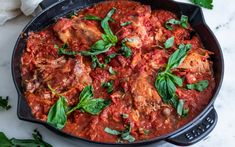 a skillet filled with meat covered in sauce and garnished with fresh herbs