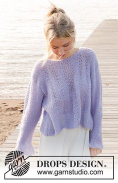 a woman wearing a purple sweater and white pants standing on a dock near the water