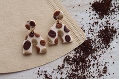 two brown and white earrings sitting on top of a piece of paper next to chocolate chips