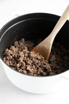 a wooden spoon in a pot filled with ground beef and spices on a white counter