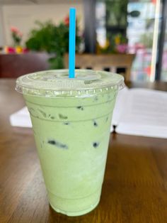 a green drink with two blue straws in it sitting on a table next to an open book