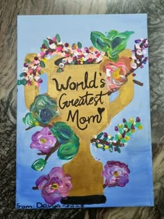 a painting with flowers on it that says, world's greatest mom in front of a golden trophy