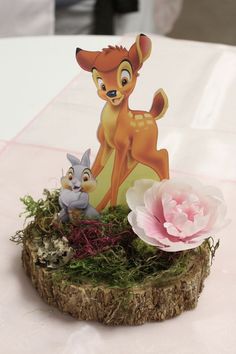 a small figurine is sitting on top of a piece of wood next to a flower