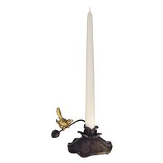 a white candle with a gold bird on it and a black flower next to it