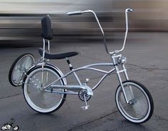 a silver bicycle parked on the side of a road next to a street with cars passing by