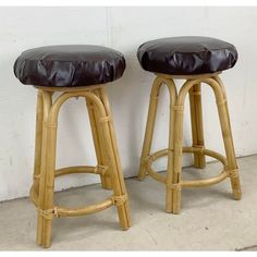 two stools made out of bamboo with black leather seat covers on them in front of a white wall