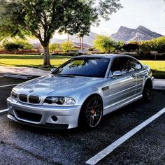 a silver car parked in a parking lot next to a tree and grass covered field