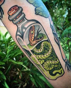 a person with a tattoo on their arm holding up a bottle that has a snake in it